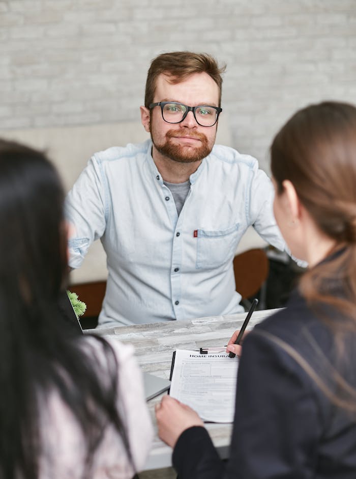 A man in glasses leads a meeting discussing documents with two women.